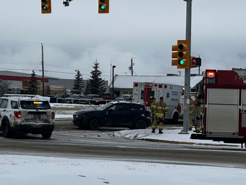 A dark vehicle seems to have hit something in a snowy intersection, an ambulance is behind it, a firetruck is beside it and an RCMP SUV is in front of it. A couple of firefighters stand next to the vehicle.