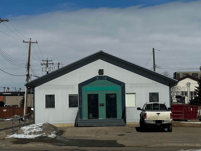 A photo of a grey building with a large green entryway with snow in the parking lot and a white truck out front.