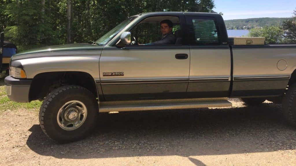 A green and grey dodge truck with a young man sitting in the driver's seat.
