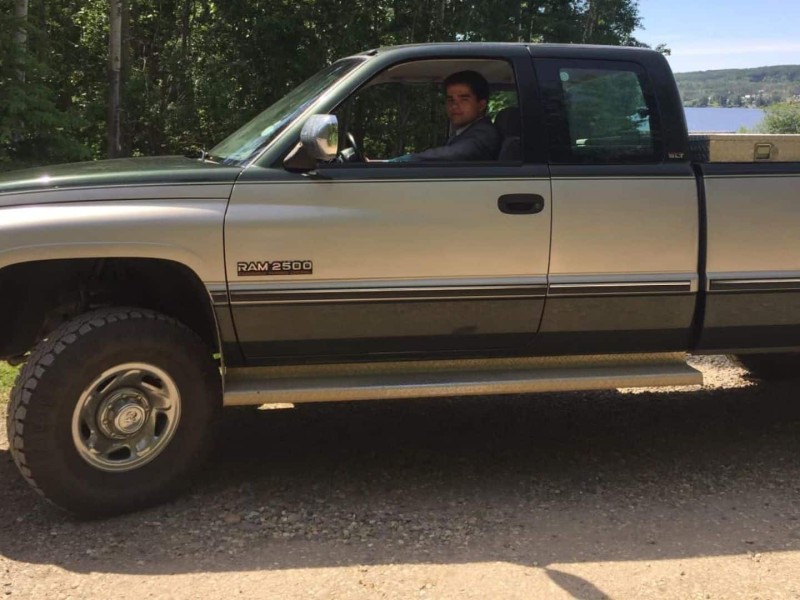 A green and grey dodge truck with a young man sitting in the driver's seat.