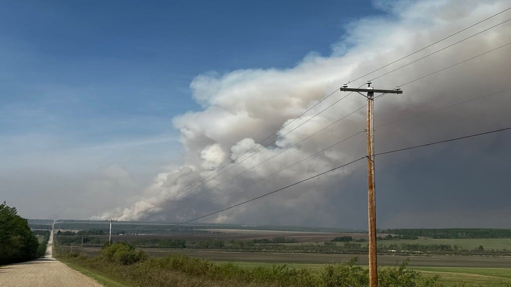 Wildfire smoke in the distance from a dirt road that heads towards it.