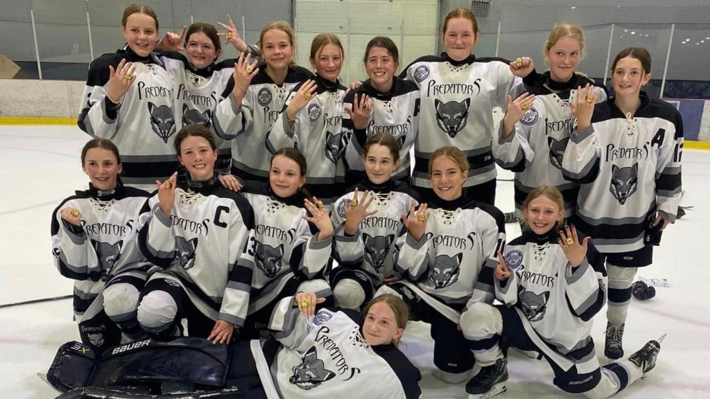 A team of preteen hockey players on the ice showing off their gold rings after the tournament.