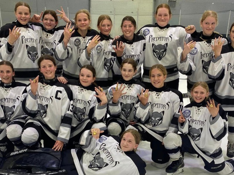 A team of preteen hockey players on the ice showing off their gold rings after the tournament.