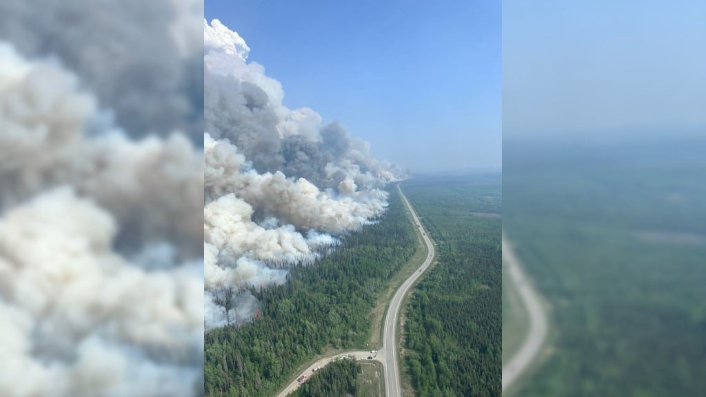 An aerial shot of the Stoddart Creek wildfire smoke coming out of a swath of trees cut through by a road.