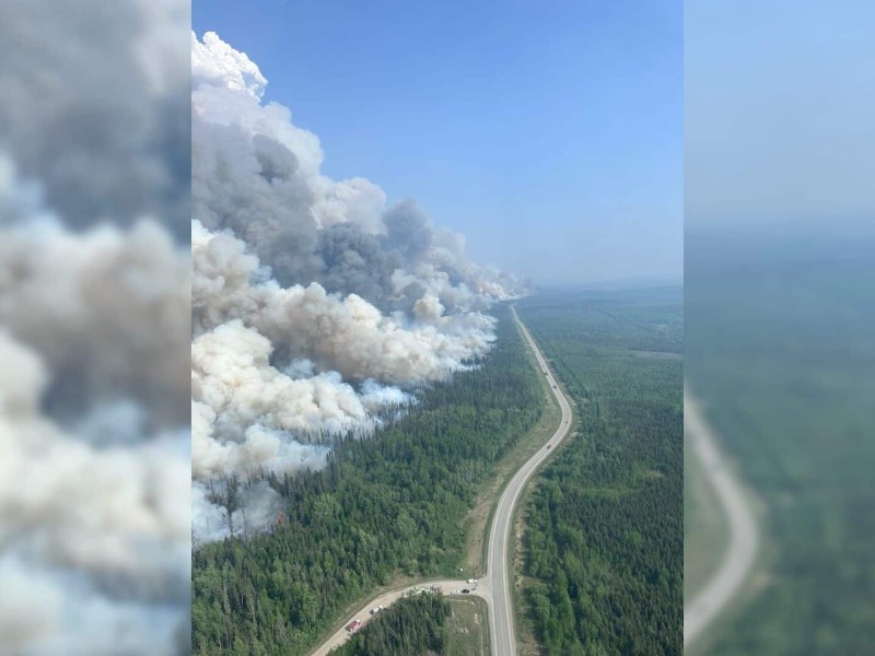 An aerial shot of the Stoddart Creek wildfire smoke coming out of a swath of trees cut through by a road.