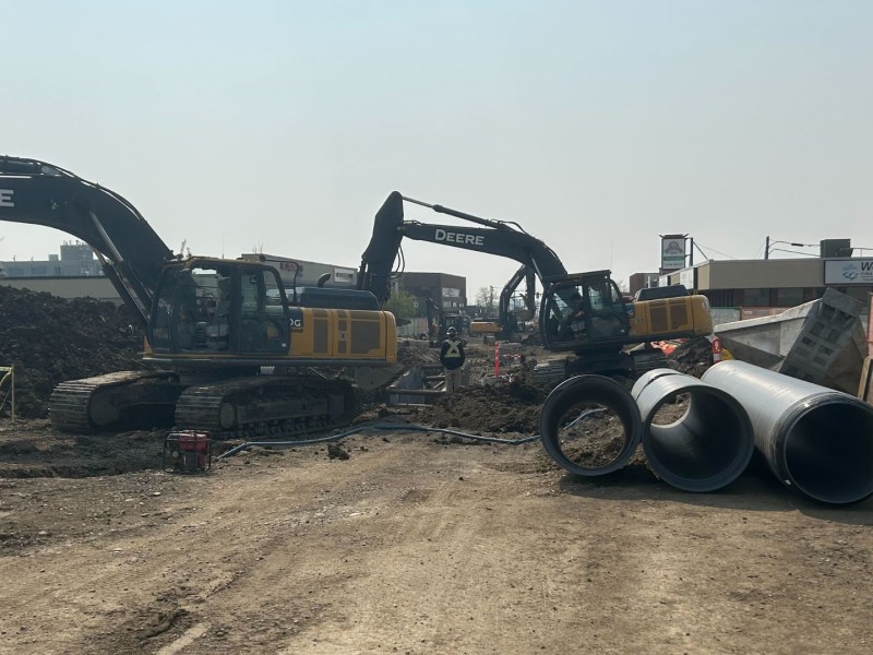 A picture of a dirt road with construction vehicles and people working, with some pipes off to the side.