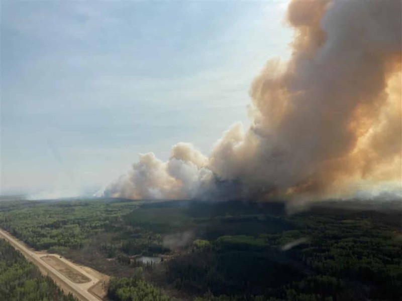 An aerial view of a lot of forest land with smoke covering half the sky coming from a distant wildfire.