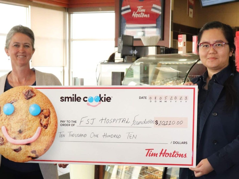 Two women holding a huge cheque with a cookie on it.