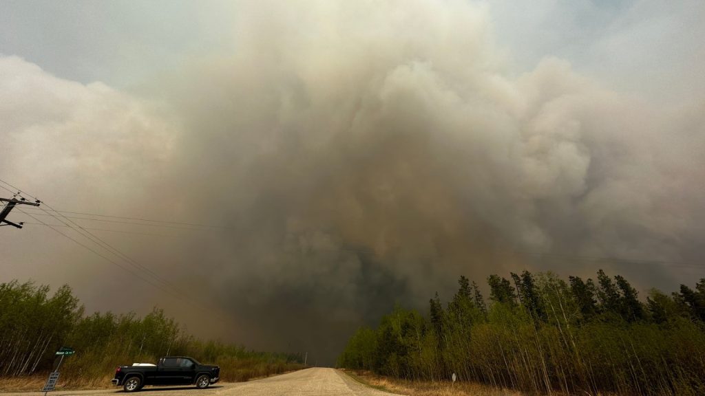 A picture of smoke above a dirt road and trees with a black truck on the road.