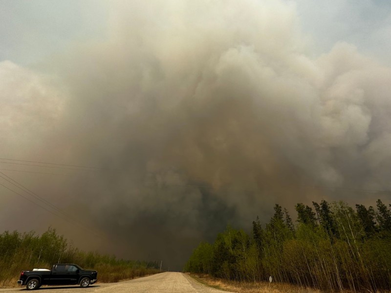A picture of smoke above a dirt road and trees with a black truck on the road.