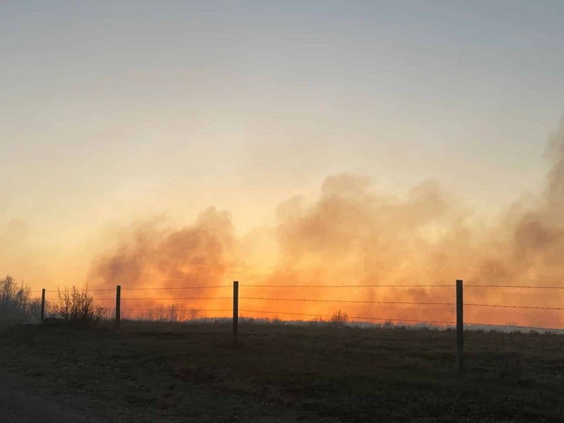A picture of a barbed wire fence backlit by a sunset with smoke.