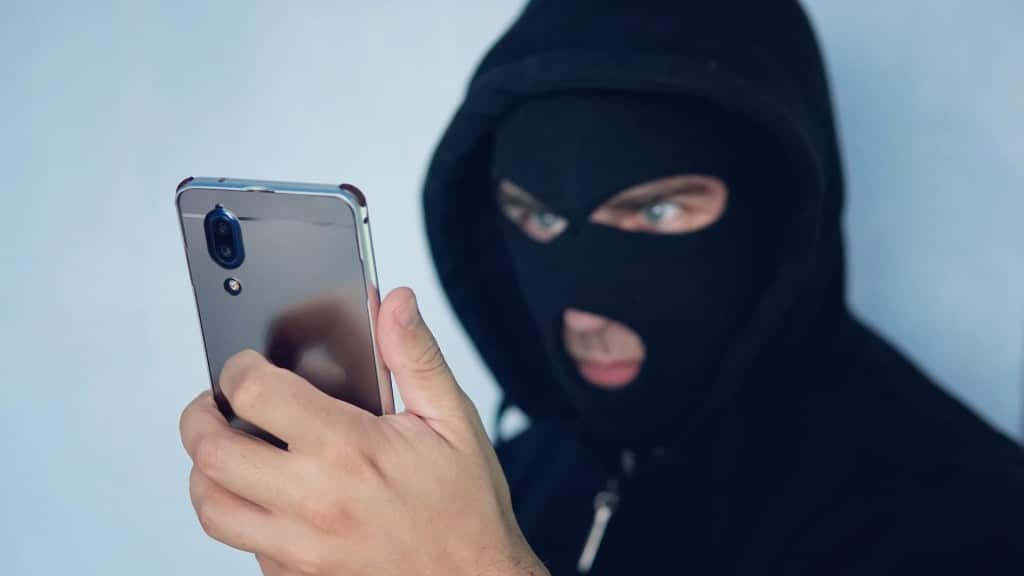 A masked man holding a smart phone.