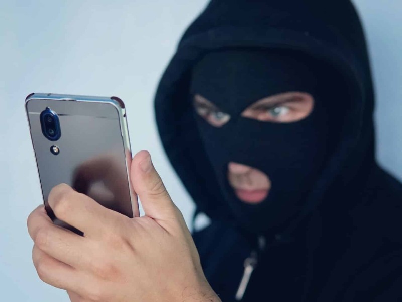 A masked man holding a smart phone.