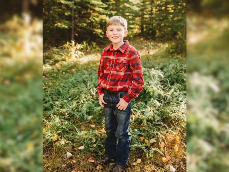 A picture of a young boy in plaid and dark jeans standing in a forest.