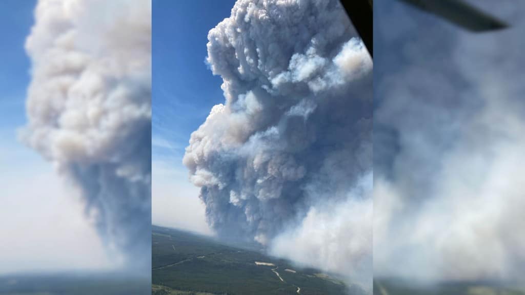 Aerial shot of a lot of smoke going into a blue sky over a flat, green landscape.