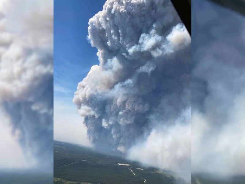 Aerial shot of a lot of smoke going into a blue sky over a flat, green landscape.