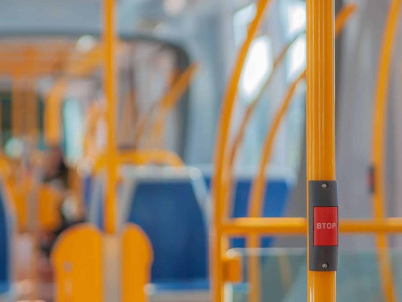 The interior of a bus with blue seats and yellow handles. A stop button is attached to the closest handle.