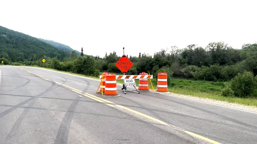 A road closure and forest fire sign on a highway with wildfire smoke in the area.