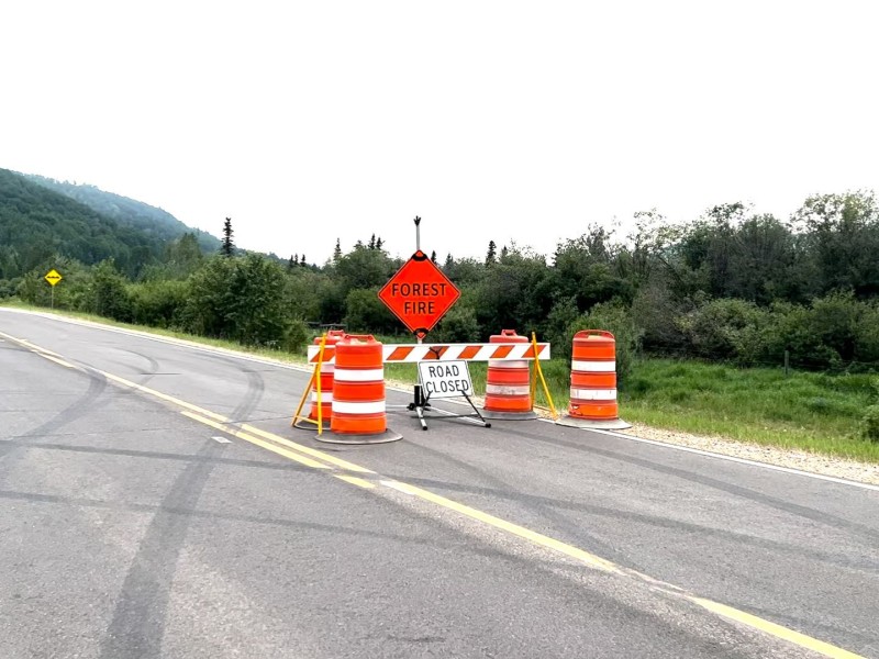 A road closure and forest fire sign on a highway with wildfire smoke in the area.