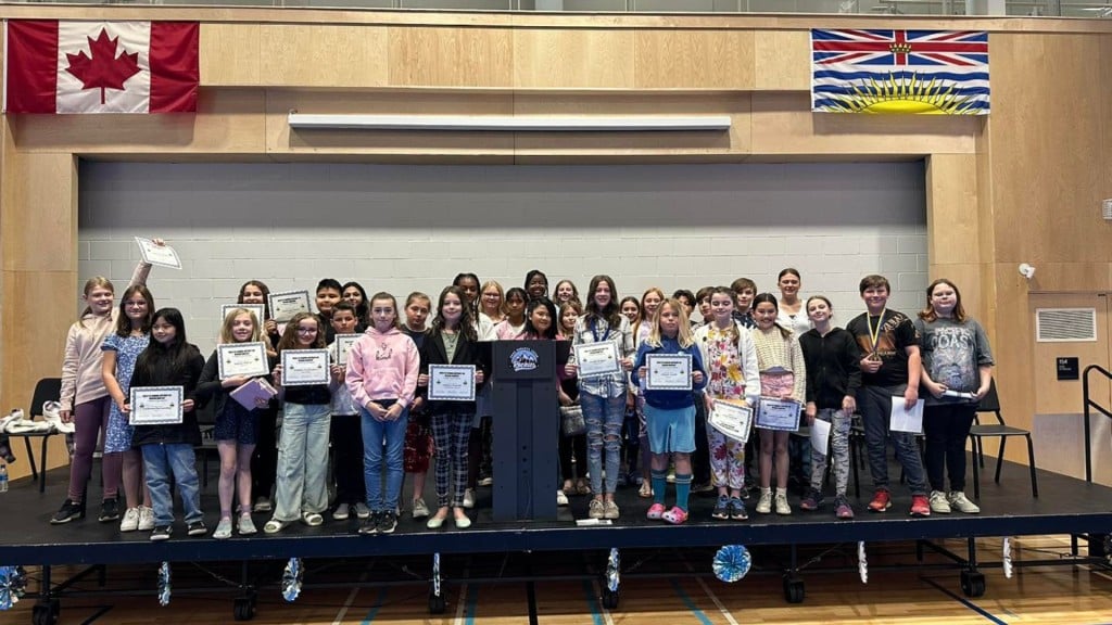 A group of students with a few holding certificates on stage underneath a Canada and B.C. flag.