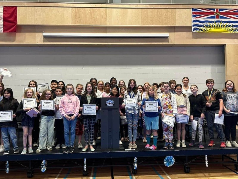 A group of students with a few holding certificates on stage underneath a Canada and B.C. flag.