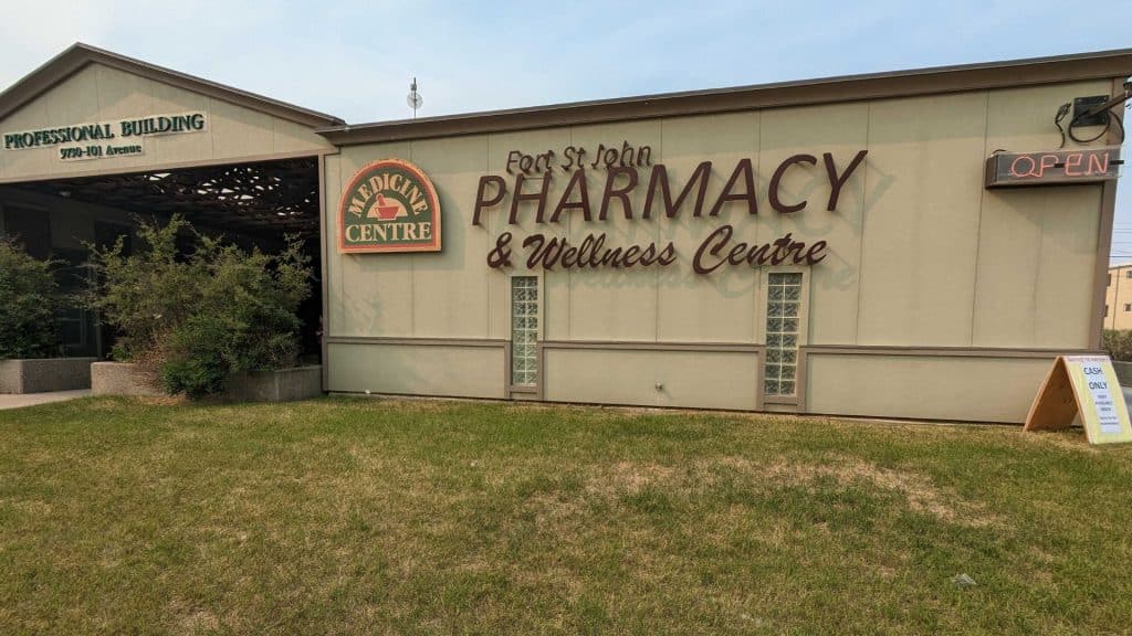 A grey building with a sign that reads Medicine Centre and Fort St. John Pharmacy & Wellness Centre on the front.