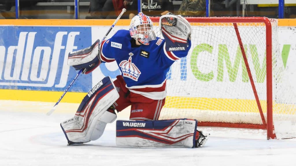 A hockey goalie raising his glove to make a save on the ice.