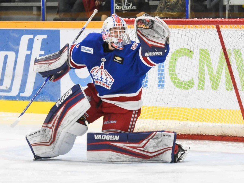 A hockey goalie raising his glove to make a save on the ice.