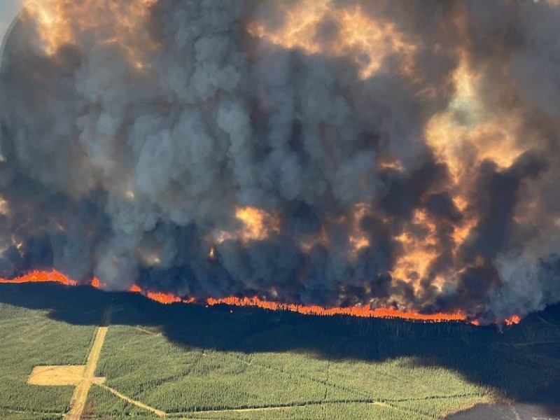 An aerial shot of a wildfire going through a forest with smoke billowing into the sky.