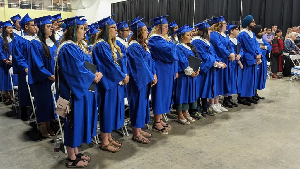 Graduates in teal gowns standing up.
