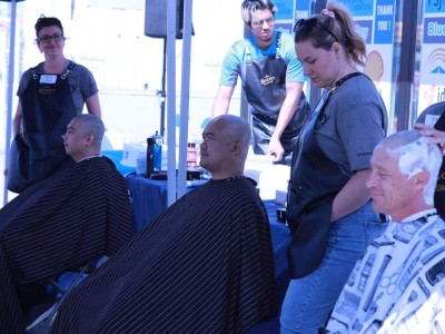 Three men in barber's capes with newly shaved heads and hair dressers behind them.