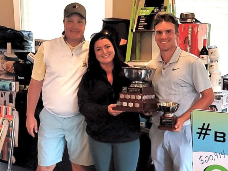 Three people smiling at the camera, two of them holding trophies