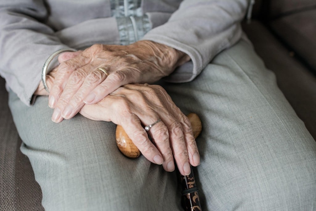 A image of an older person clasping their hands on their lap. 