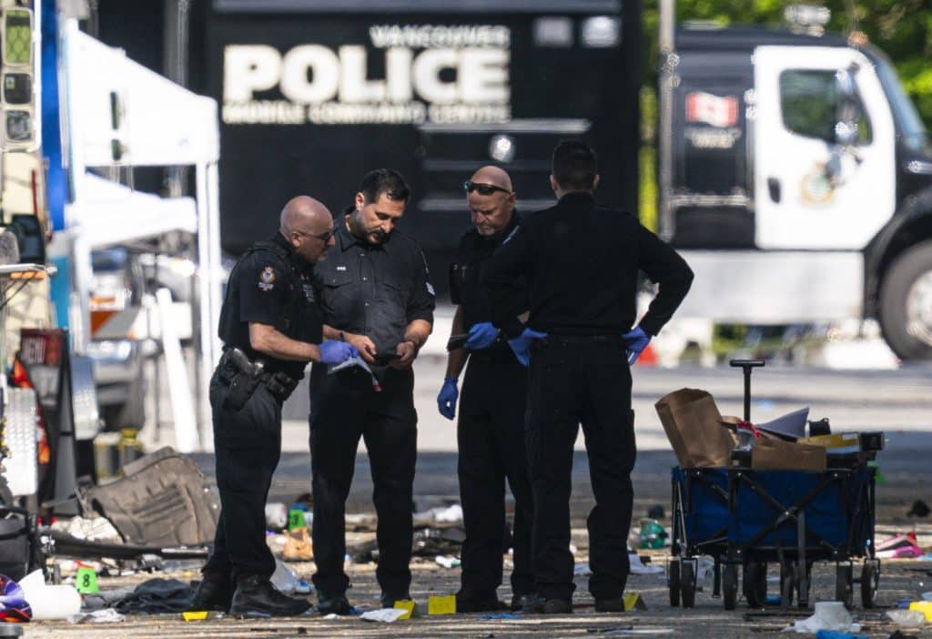 Members of the Vancouver Police forensics team examine a victim's phone while investigating the scene where a vehicle drove into crowd at a street festival Saturday evening in Vancouver, Sunday, April 27, 2025.