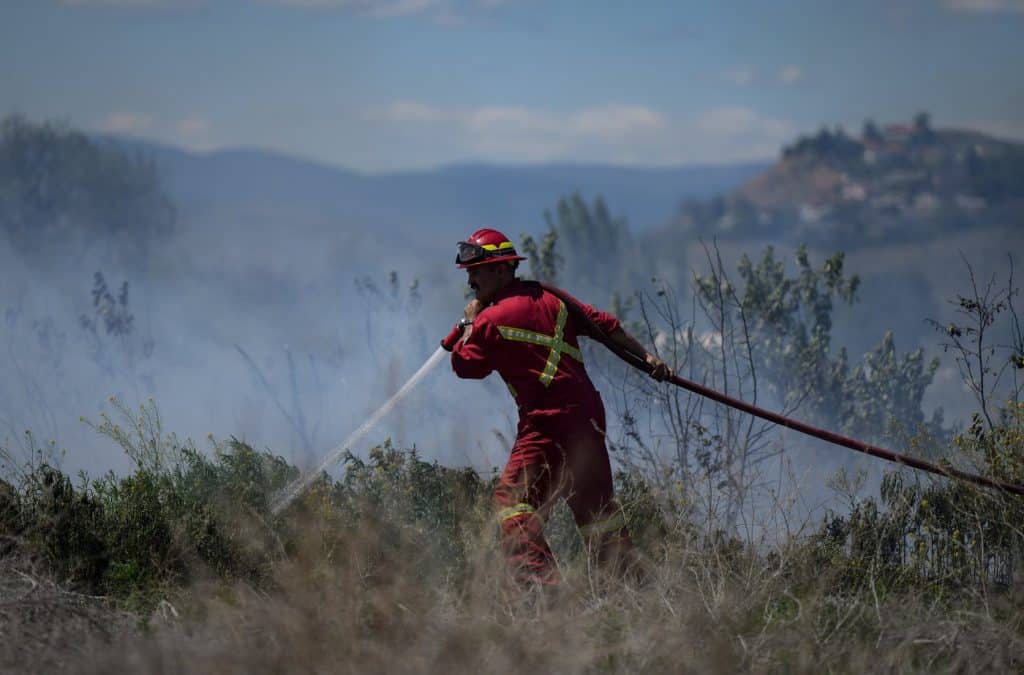 A firefighter directs water on a grass fire burning on an acreage behind a residential property in Kamloops on June 5th, 2023. (THE CANADIAN PRESS/Darryl Dyck)