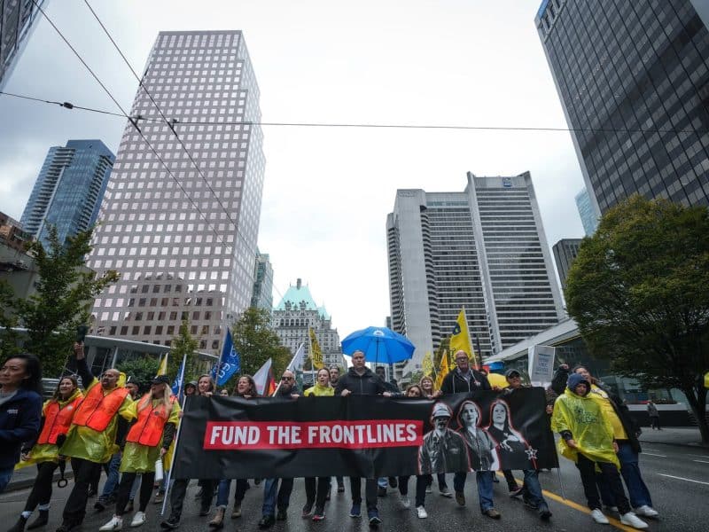BC General Employees' Union President Paul Finch, centre, helps carry a banner as BCGEU members and supporters march to a rally in Vancouver on October 1st, 2025. (THE CANADIAN PRESS/Darryl Dyck)