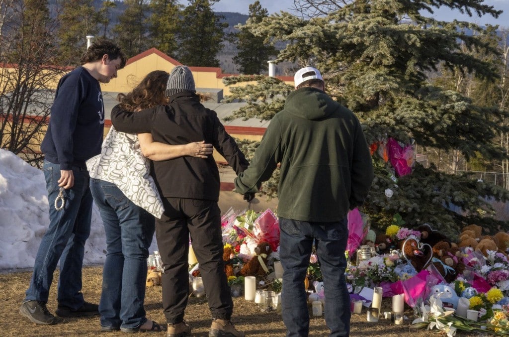Residents hug as they place flowers at a memorial for the victims of a mass shooting in Tumbler Ridge, B.C., on Thursday, Feb. 12, 2026. THE CANADIAN PRESS/Christinne Muschi