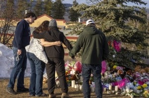 Residents hug as they place flowers at a memorial for the victims of a mass shooting in Tumbler Ridge, B.C., on Thursday, Feb. 12, 2026. THE CANADIAN PRESS/Christinne Muschi