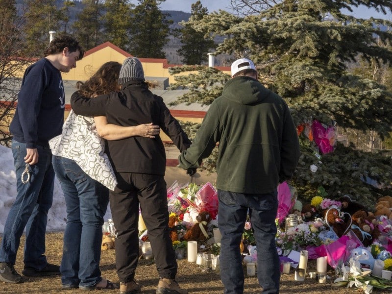 Residents hug as they place flowers at a memorial for the victims of a mass shooting in Tumbler Ridge, B.C., on Thursday, Feb. 12, 2026. THE CANADIAN PRESS/Christinne Muschi