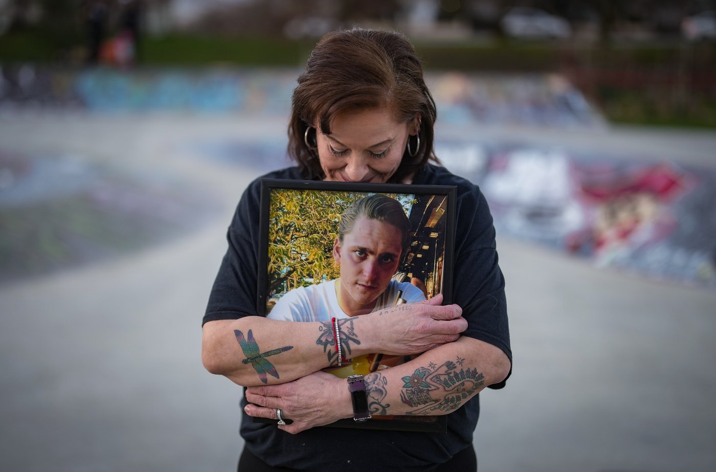 Meredith Dan holds a photo of her late son Glenn Rebic, who died of a fentanyl overdose in 2019 at the age of 29, while posing for a photograph at the China Creek skate park where he used to skateboard, in Vancouver, on Friday, March 13, 2026. THE CANADIAN PRESS/Darryl Dyck