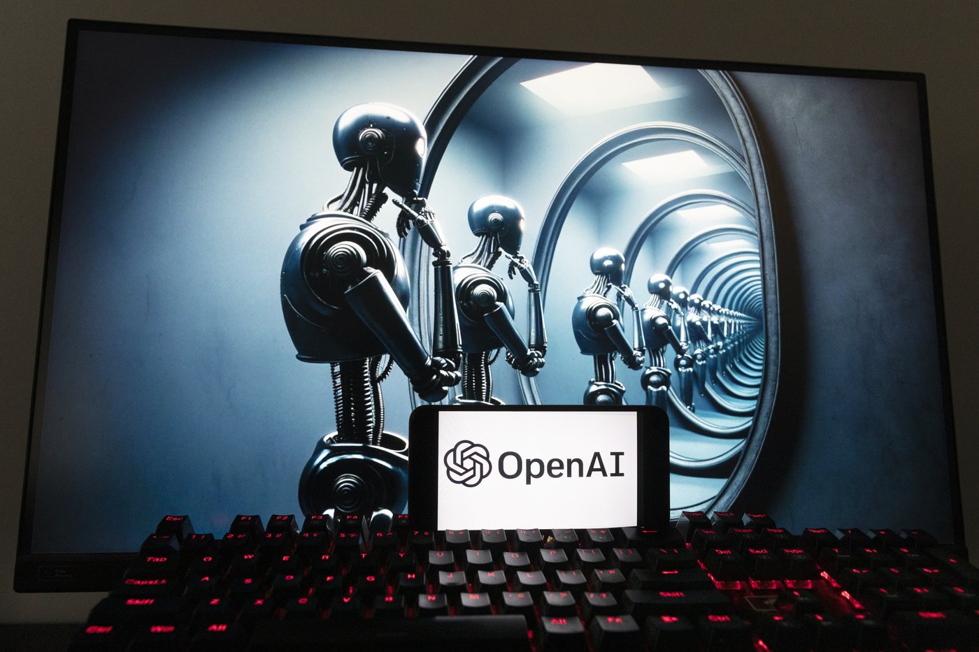 The OpenAI logo is seen displayed on a cellphone with an image on a computer screen generated by ChatGPT's Dall-E text-to-image model, Friday, Dec. 8, 2023, in Boston. (AP Photo/Michael Dwyer)