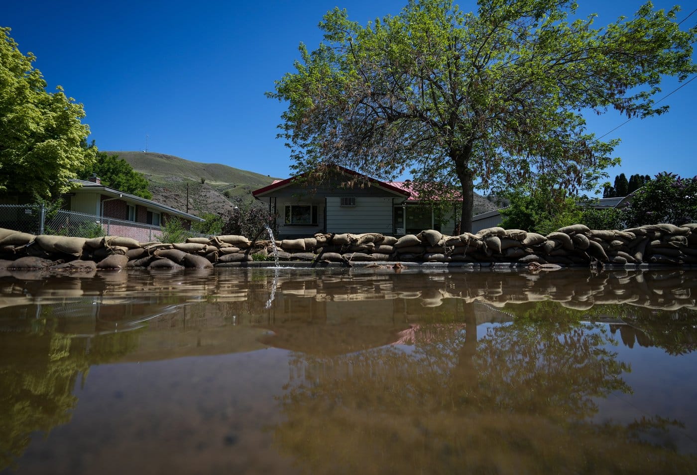 Emergency officials in British Columbia are warning of flooding along the Columbia River in the southeastern corner of the province bordering Alberta. Water is pumped out from a flooded home near the Bonaparte River as sandbags line a sidewalk in Cache Creek, B.C., on Sunday, May 14, 2023. THE CANADIAN PRESS/Darryl Dyck