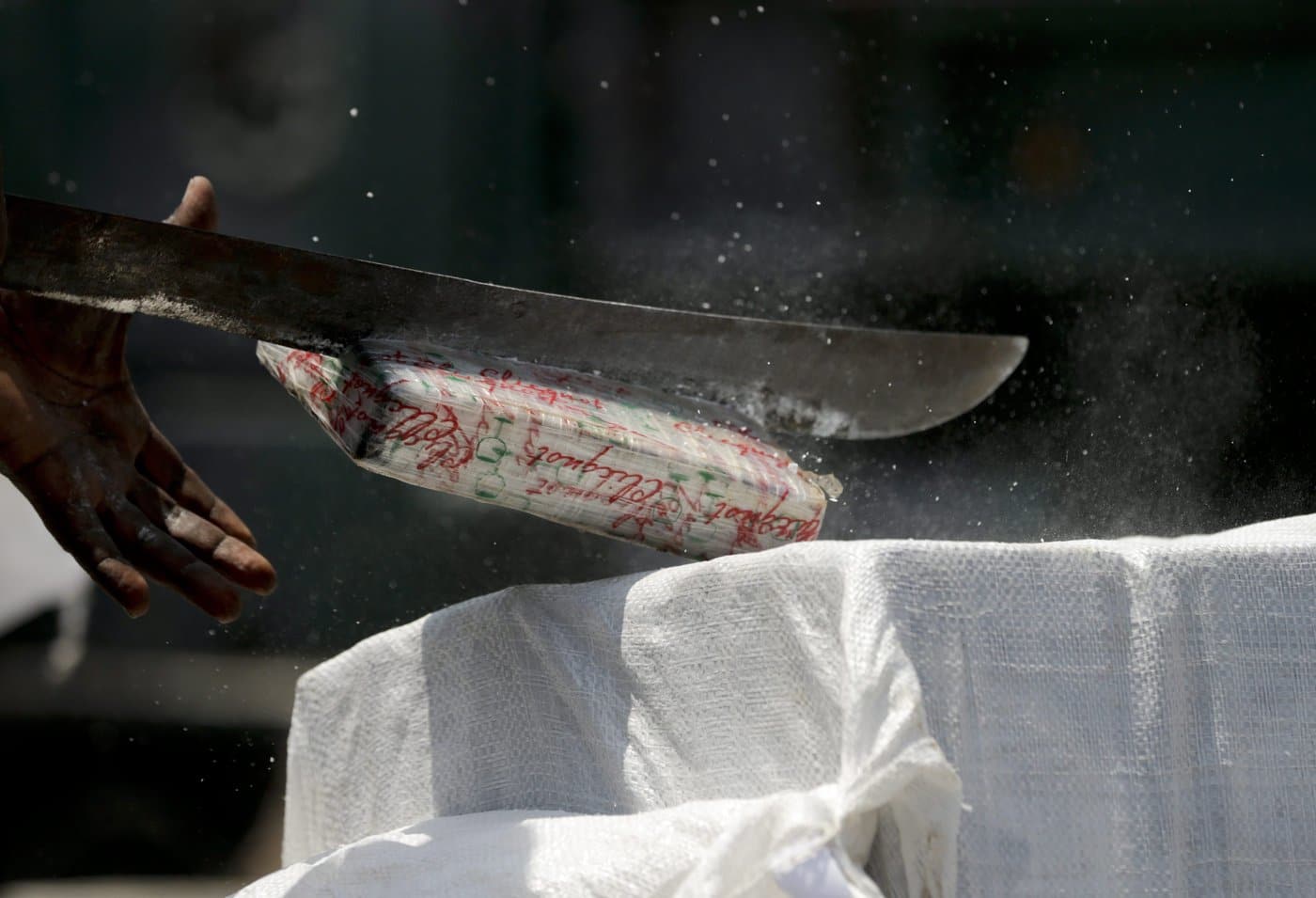 A narcotics agent uses a machete to slice open a brick of cocaine, as part of an operation to destroy seized drugs, on the outskirts of Panama City, Friday, April 1, 2016. (AP Photo/Arnulfo Franco)